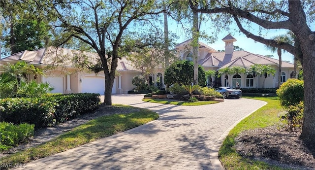 mediterranean / spanish home featuring a garage, decorative driveway, a tile roof, and stucco siding