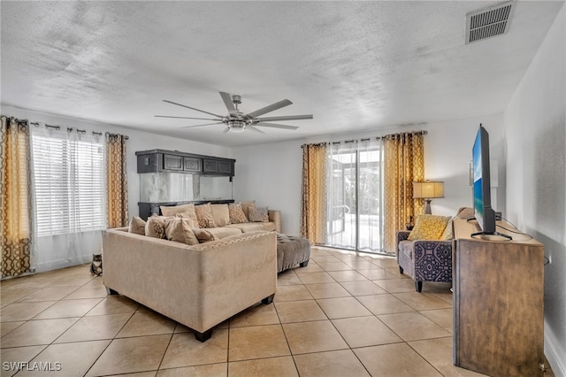 living room featuring a ceiling fan, visible vents, a textured ceiling, and light tile patterned floors