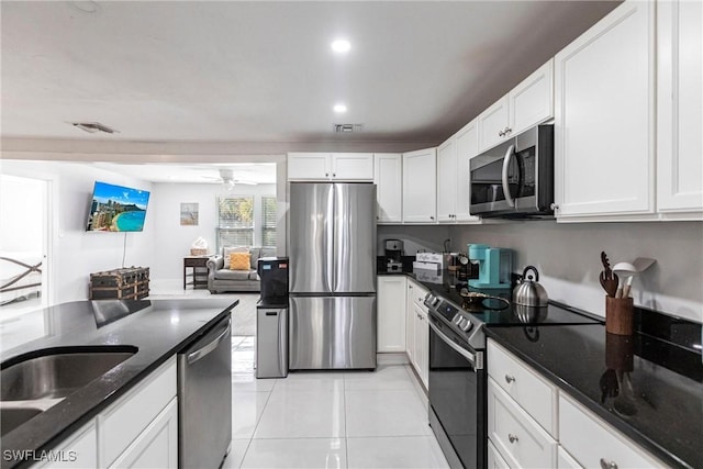 kitchen with dark stone countertops, appliances with stainless steel finishes, light tile patterned floors, ceiling fan, and white cabinets