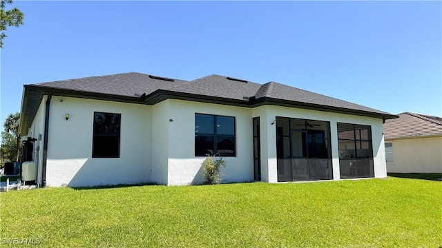 rear view of property featuring roof with shingles, a lawn, a sunroom, and stucco siding