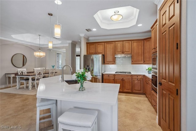 kitchen with light countertops, appliances with stainless steel finishes, brown cabinetry, and a raised ceiling