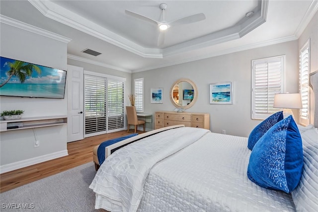 bedroom featuring crown molding, visible vents, a tray ceiling, and wood finished floors