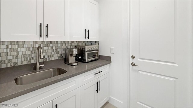 kitchen with dark countertops, white cabinetry, backsplash, and a sink