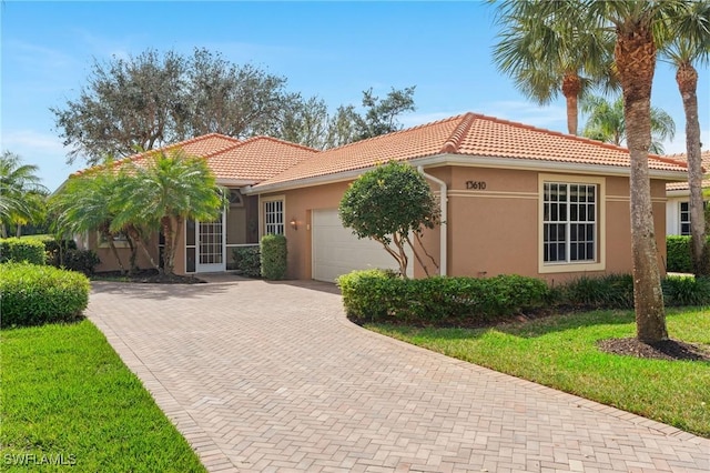 view of front of home with decorative driveway, stucco siding, an attached garage, a tiled roof, and a front lawn