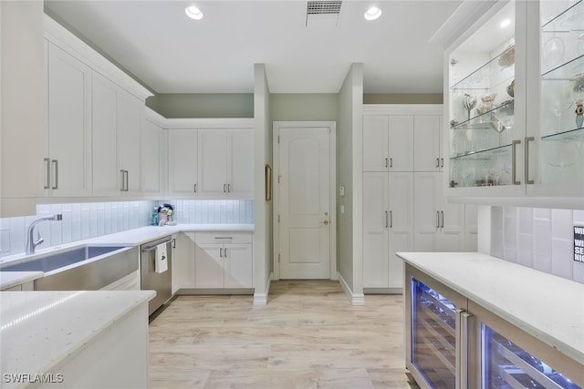 kitchen featuring dishwasher, light wood-style flooring, backsplash, white cabinetry, and a sink