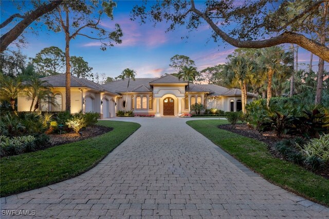 12303 Colliers Reserve Dr, Naples, FL 34110 - mediterranean / spanish-style home with curved driveway, an attached garage, stucco siding, and a front yard