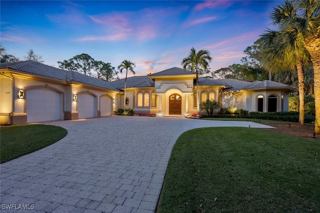 mediterranean / spanish home featuring an attached garage, stucco siding, decorative driveway, and a front yard