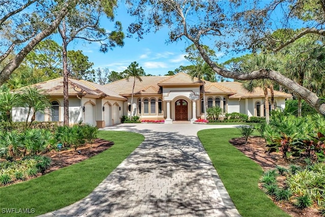 mediterranean / spanish-style home with a garage, a tiled roof, decorative driveway, and stucco siding