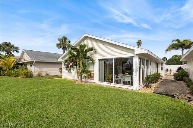 rear view of house featuring a sunroom, fence, and a lawn