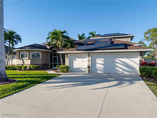 view of front of house featuring an attached garage, solar panels, concrete driveway, stucco siding, and a front yard