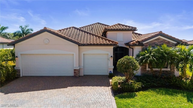 mediterranean / spanish house with stone siding, a tiled roof, an attached garage, decorative driveway, and stucco siding