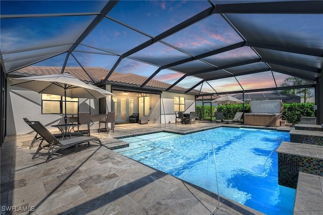 pool at dusk with a lanai, a patio area, and a hot tub