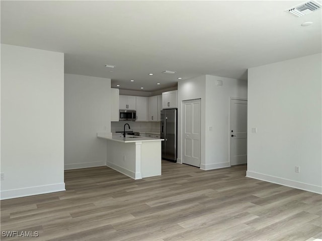 kitchen with white cabinetry, kitchen peninsula, light wood-type flooring, sink, and appliances with stainless steel finishes