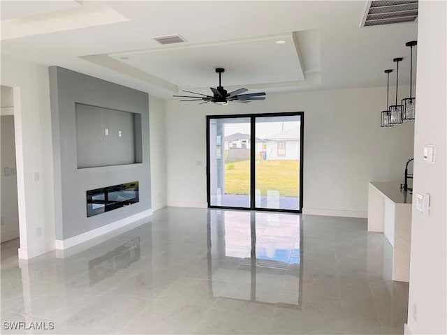 unfurnished living room featuring a glass covered fireplace, a raised ceiling, visible vents, and baseboards