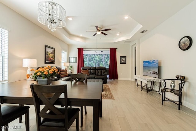 dining room featuring ceiling fan with notable chandelier, light hardwood / wood-style floors, and a raised ceiling