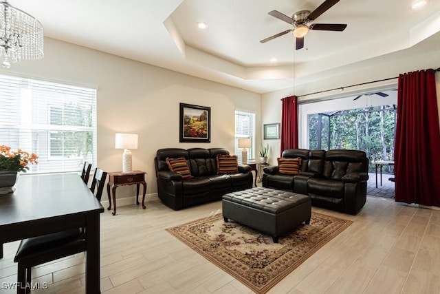 living room featuring ceiling fan with notable chandelier, light hardwood / wood-style flooring, and a raised ceiling