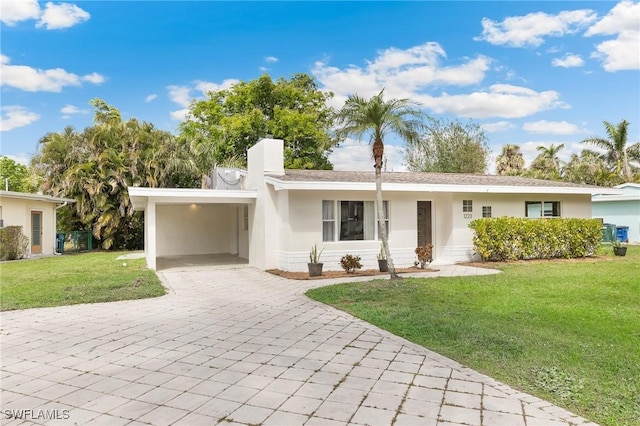 ranch-style house featuring decorative driveway, stucco siding, a carport, a front lawn, and a chimney