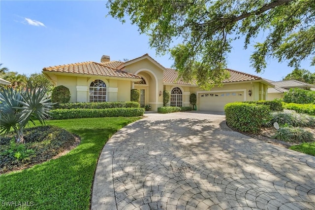 mediterranean / spanish-style home featuring a chimney, a tiled roof, an attached garage, decorative driveway, and stucco siding