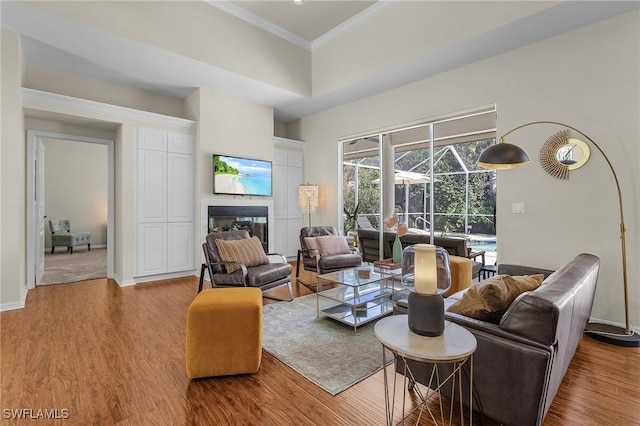 living area with wood finished floors, a sunroom, baseboards, a glass covered fireplace, and crown molding