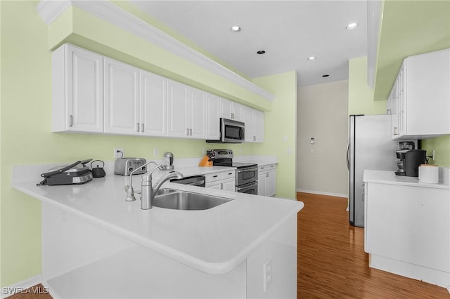 kitchen featuring appliances with stainless steel finishes, white cabinets, a sink, wood finished floors, and a peninsula