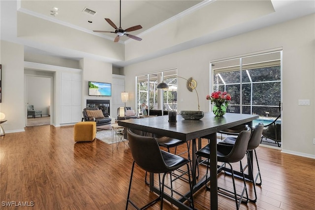 dining space featuring crown molding, visible vents, a glass covered fireplace, wood finished floors, and baseboards