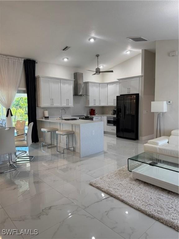 kitchen featuring black refrigerator with ice dispenser, white cabinetry, a kitchen breakfast bar, wall chimney exhaust hood, and an island with sink