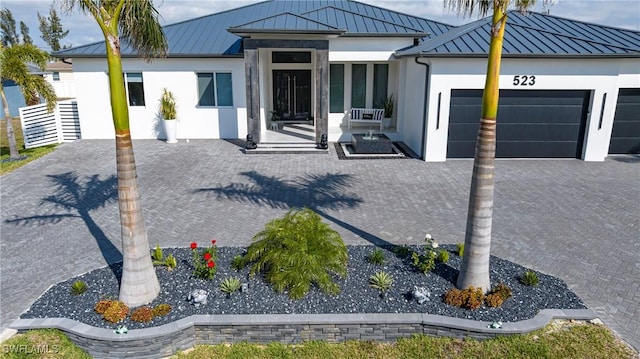 view of front of home featuring decorative driveway, stucco siding, a standing seam roof, metal roof, and a garage