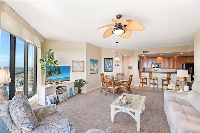 living area with baseboards, ceiling fan, visible vents, and light colored carpet