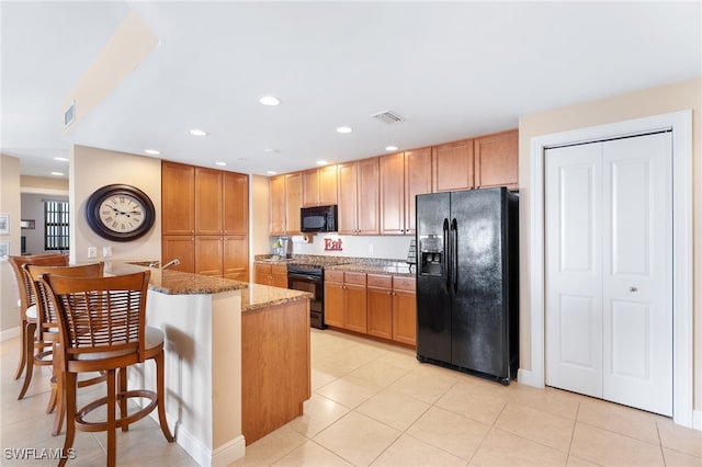 kitchen with light stone countertops, black appliances, a breakfast bar area, and brown cabinetry