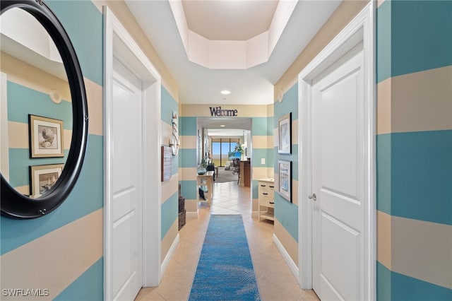 hall featuring a tray ceiling, baseboards, and light tile patterned floors