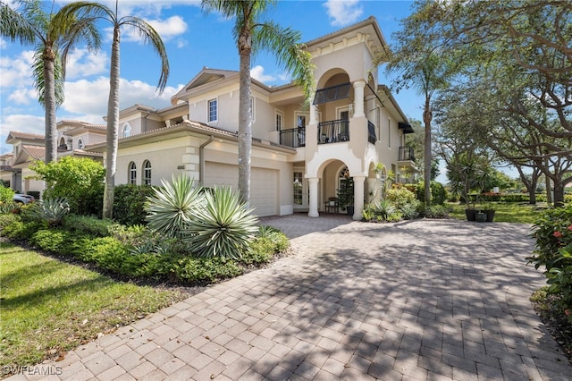 mediterranean / spanish home featuring an attached garage, a balcony, a tile roof, decorative driveway, and stucco siding