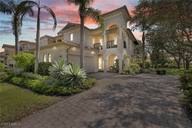 mediterranean / spanish house with a balcony, decorative driveway, stucco siding, a tile roof, and a garage