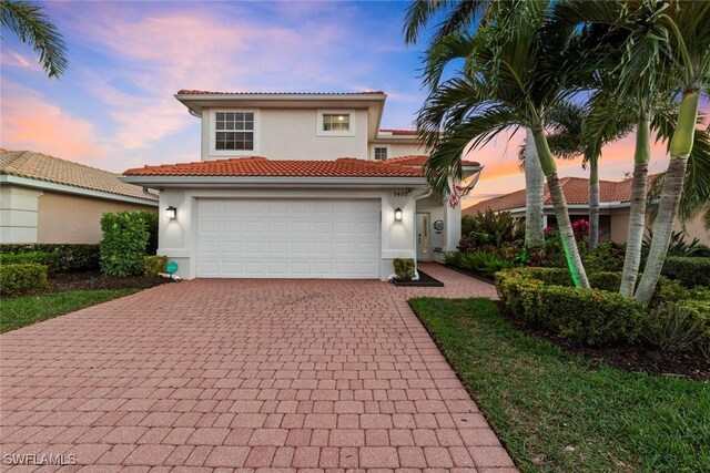 mediterranean / spanish house featuring a tiled roof, decorative driveway, and stucco siding