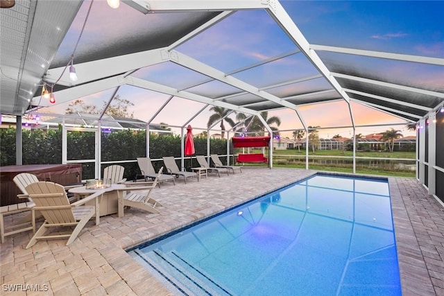 pool at dusk with an outdoor pool, a lanai, and a patio area