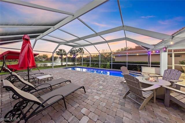 pool at dusk featuring glass enclosure, a patio area, an outdoor pool, and a fire pit