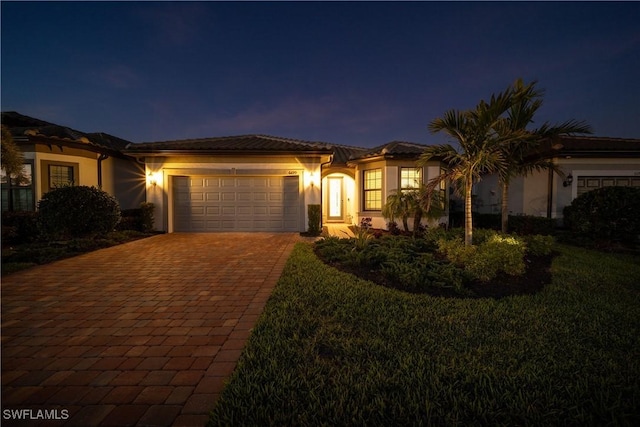 view of front of home with a yard, decorative driveway, an attached garage, and stucco siding