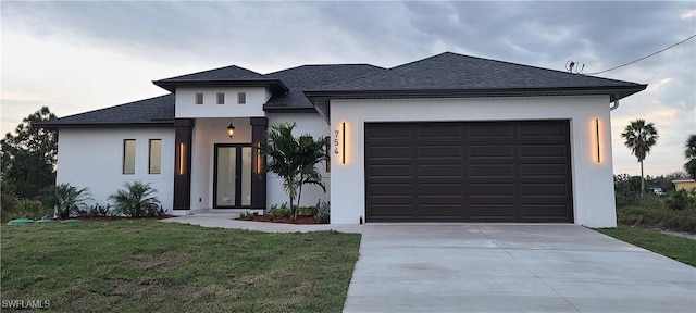 prairie-style home with driveway, roof with shingles, a front lawn, and stucco siding