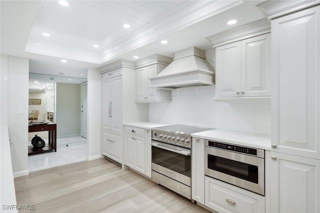 kitchen featuring stainless steel stove, white cabinets, light countertops, a raised ceiling, and custom range hood