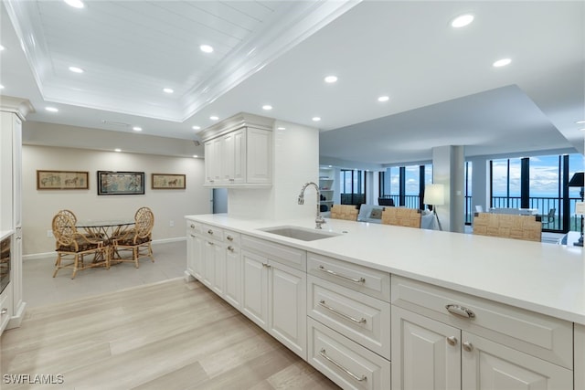 kitchen with a tray ceiling, white cabinets, light countertops, and a sink