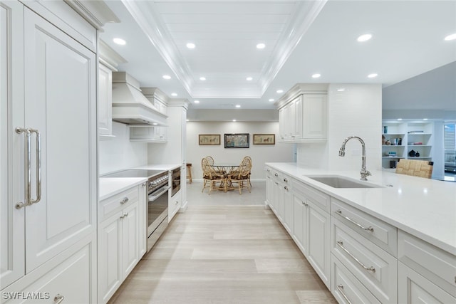 kitchen featuring high end stove, a sink, white cabinets, light countertops, and custom exhaust hood