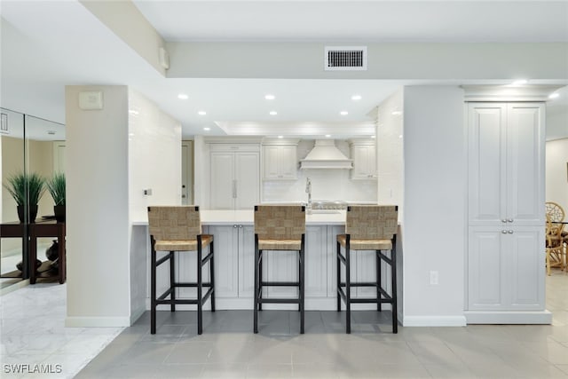 kitchen with premium range hood, a breakfast bar, visible vents, white cabinets, and light countertops