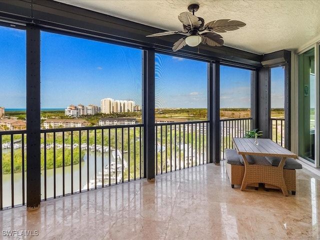 sunroom with ceiling fan and a water view