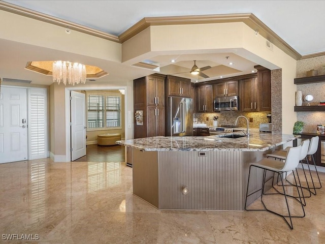 kitchen with a breakfast bar area, stainless steel appliances, a sink, light stone countertops, and a peninsula