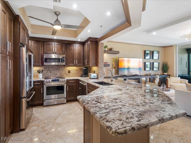 kitchen with stainless steel appliances, a raised ceiling, a sink, and a peninsula