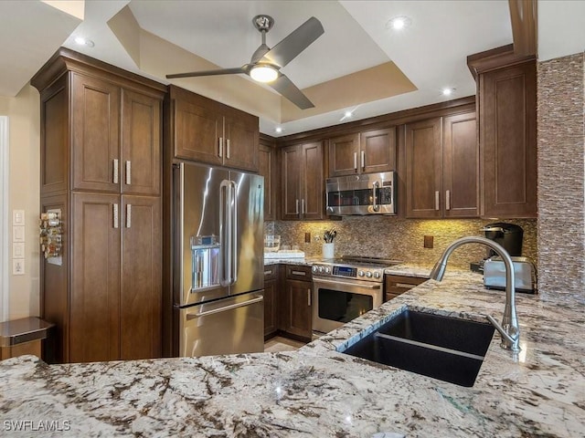 kitchen with a ceiling fan, appliances with stainless steel finishes, backsplash, light stone counters, and a sink