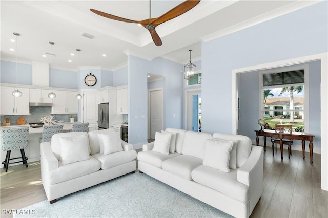 living room with ceiling fan with notable chandelier, ornamental molding, a high ceiling, and light wood-style flooring