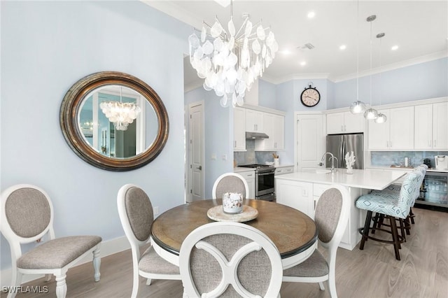 dining room with light wood finished floors, ornamental molding, and an inviting chandelier