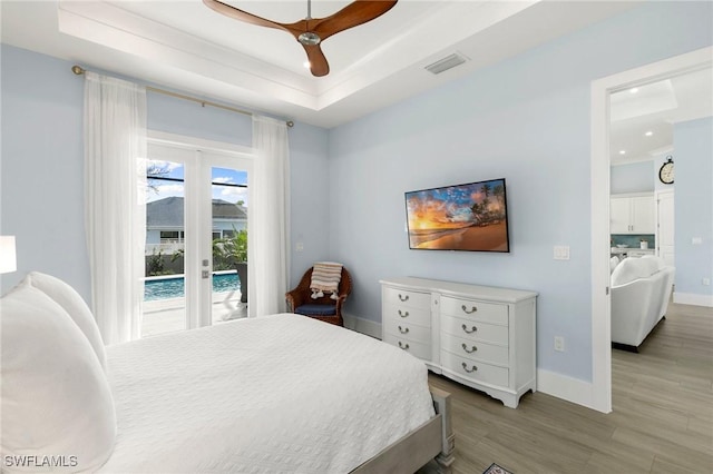 bedroom with access to exterior, a tray ceiling, visible vents, and wood finished floors