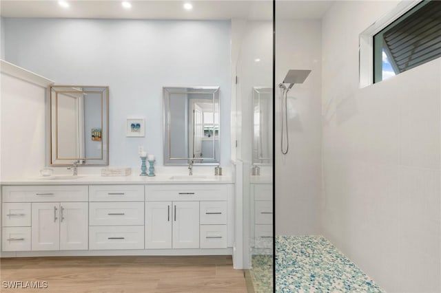 bathroom with a walk in shower, double vanity, wood finished floors, and a sink