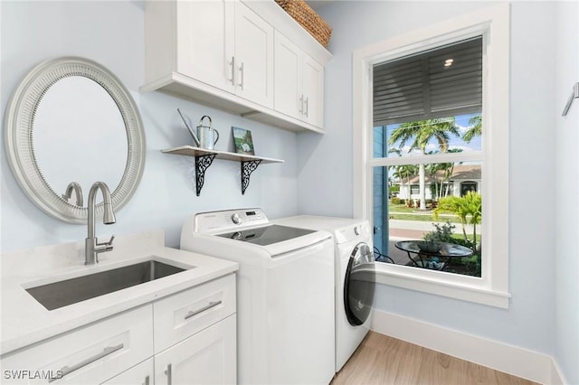 clothes washing area with cabinet space, light wood finished floors, baseboards, washing machine and clothes dryer, and a sink